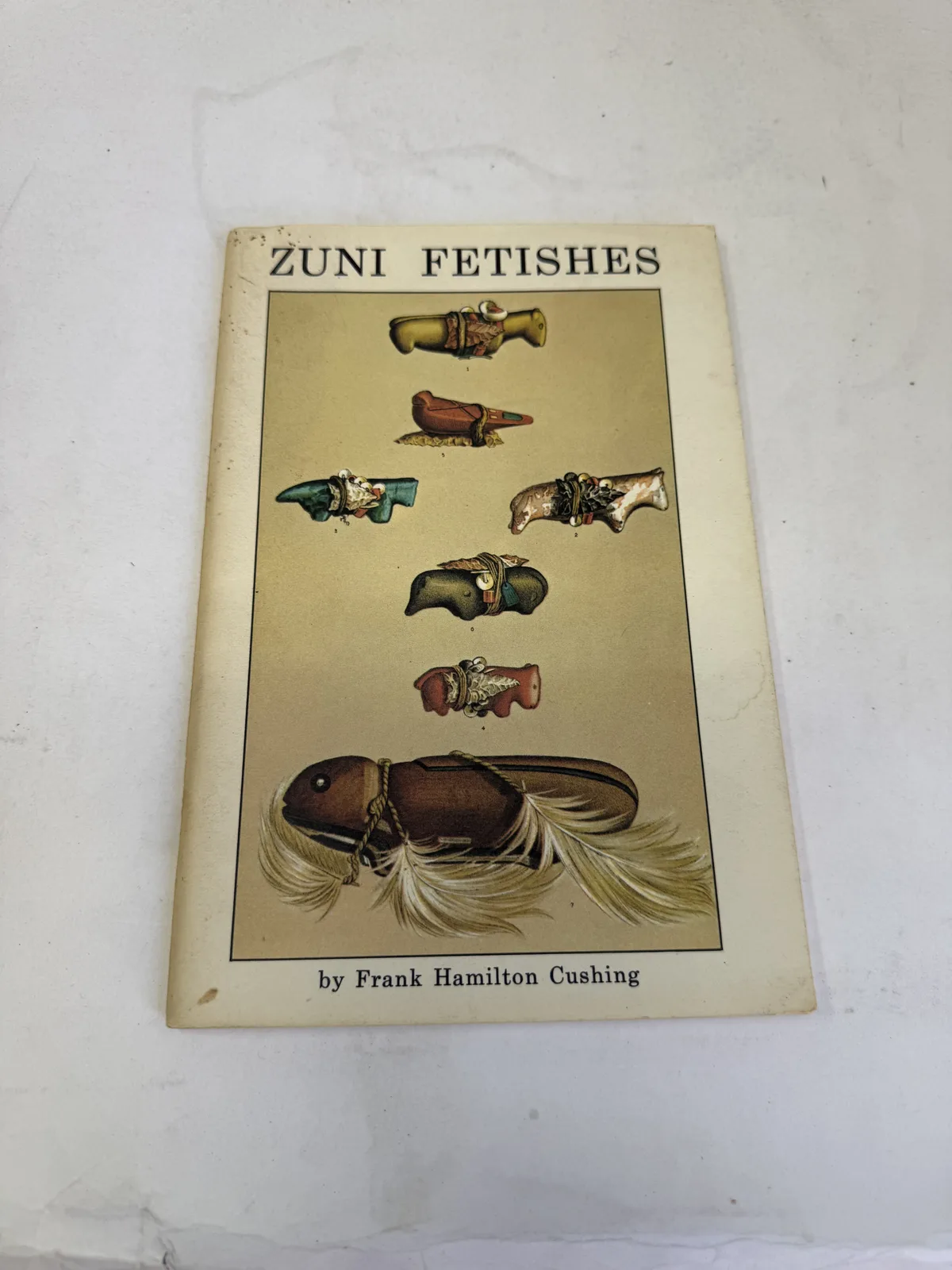 Cover of Zuni Fetishes by Frank Hamilton Cushing showing carved stone animal fetishes on a cream ground, photographed at New Mexico Literacy Project